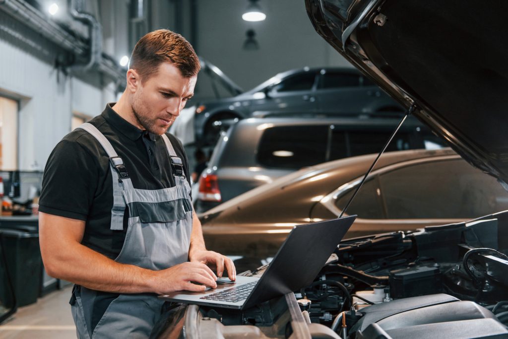 using laptop. man in uniform is working in the auto service